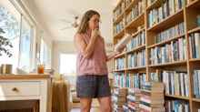 Woman standing thoughtfully in front of a bookshelf trying to choose a book