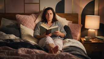 Woman frowning in bed, forcing herself through a book she doesn't want to read