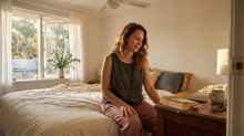 Woman sitting on the edge of her bed, looking out the window, not currently reading